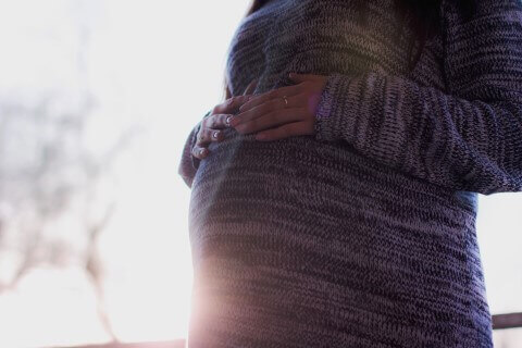 Schwangere Frau welche die Hände über ihren Babybauch hält